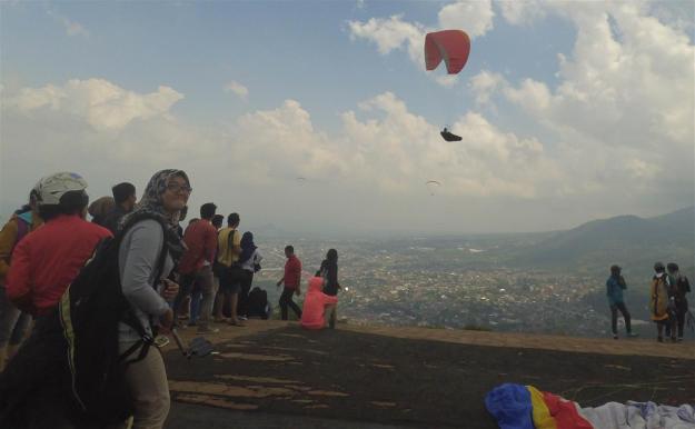 Salah satu peserta tengah bersiap-siap, dan latar belakang seseorang yang tengah terbang paralayang sendirian