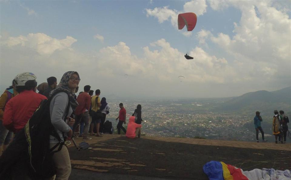 Salah satu peserta tengah bersiap-siap, dan latar belakang seseorang yang tengah paralayang sendirian